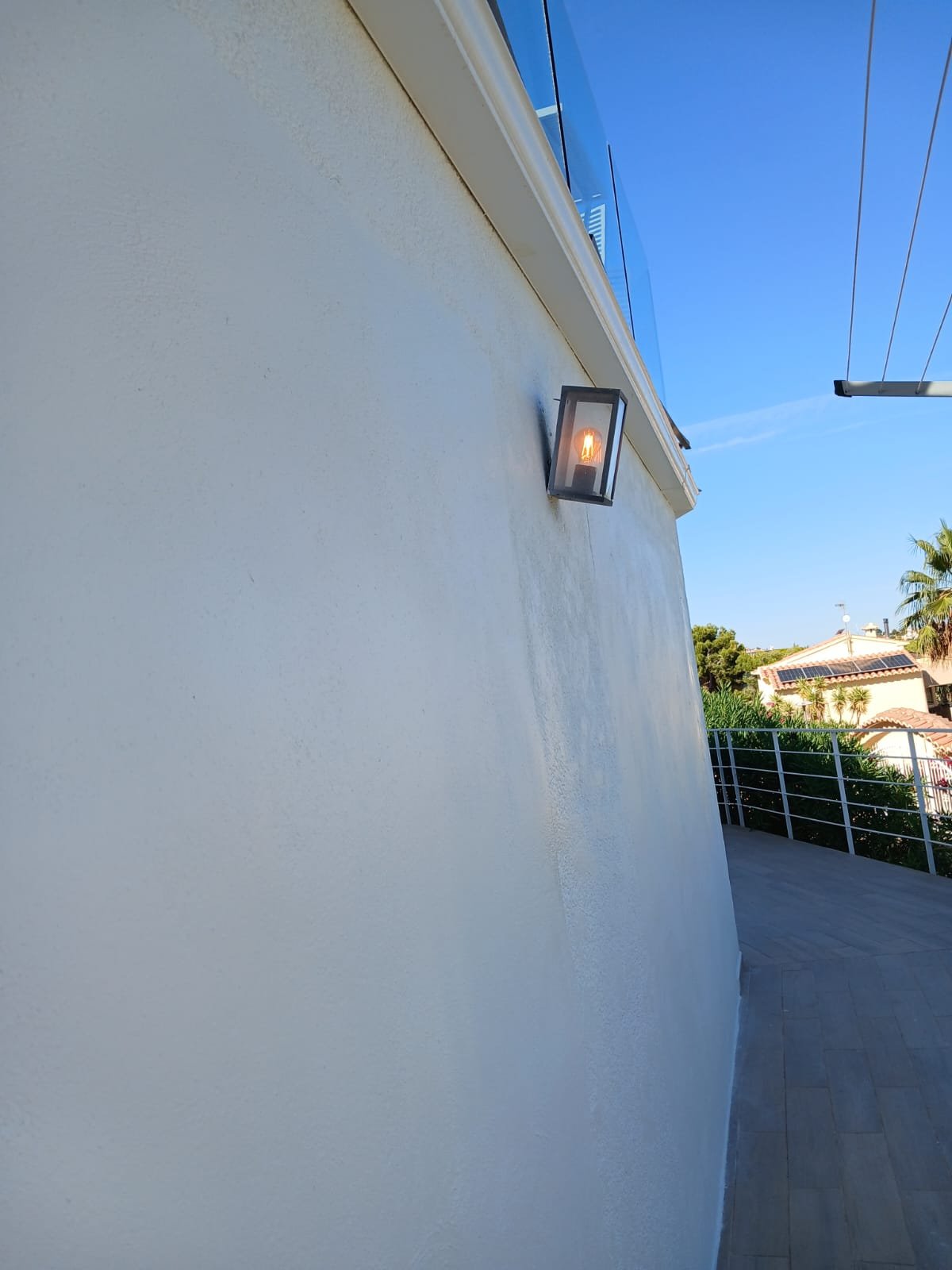 A curved exterior wall freshly painted white, with an outdoor lantern light fitting